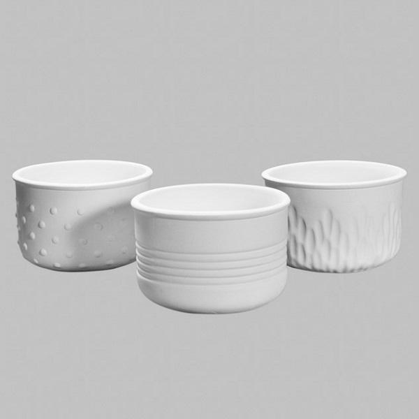 Three unglazed white ceramic bowls with textured surfaces, including dots, ridges, and wave patterns, displayed on a neutral background.