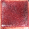 Deep red ceramic glaze sample with a glossy finish, showcasing tonal variations and a speckled texture.