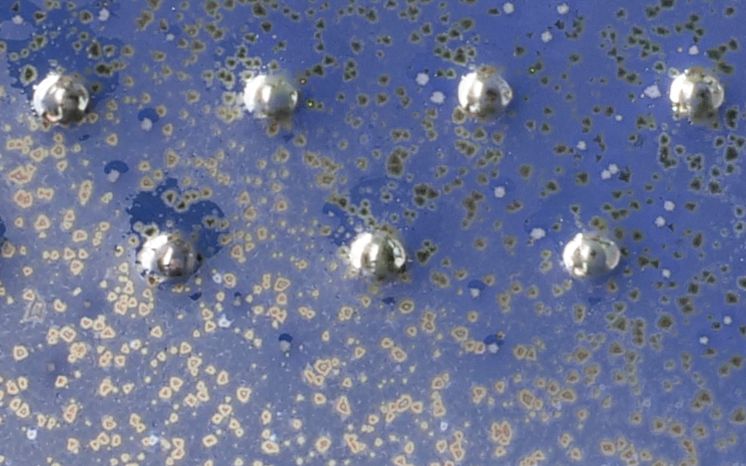 Close-up of a metallic blue ceramic glaze featuring shiny silver spheres, showcasing unique texture and decorative effects.