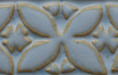 Close-up of a blue ceramic surface with embossed floral and star patterns accented by a golden glaze detail.