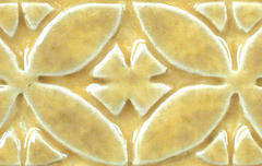 Close-up of a textured ceramic tile featuring floral patterns in a soft yellow glaze, ideal for decorative pottery projects.