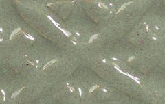 Close-up of a textured green ceramic glaze, showcasing a glossy finish and intricate surface patterns ideal for pottery.