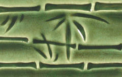 Close-up of a green ceramic tile featuring bamboo leaf patterns, showcasing detailed carving and glossy glaze finish.