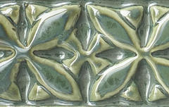 Glazed ceramic tile featuring a floral pattern in green and gold hues, showcasing texture and depth from clay decoration techniques.