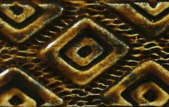 Close-up of textured clay surface with diamond patterns in earthy browns and blacks, showcasing ceramic decoration techniques.