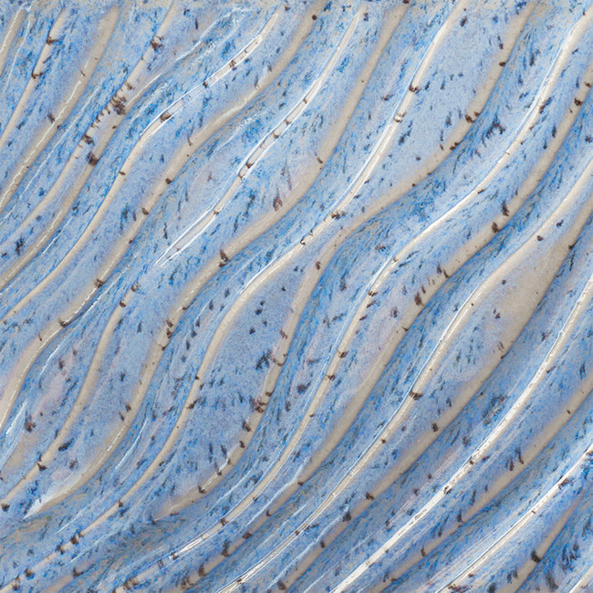 Textured blue and beige clay surface with wavy patterns, featuring flecks and depths of glaze for ceramic projects.