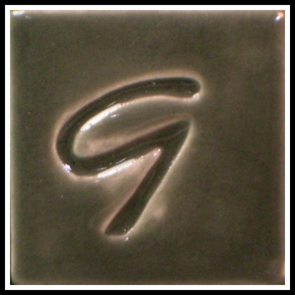 Close-up of a ceramic tile with a stylized G mark, showcasing smooth, glossy glaze in a rich brown finish.