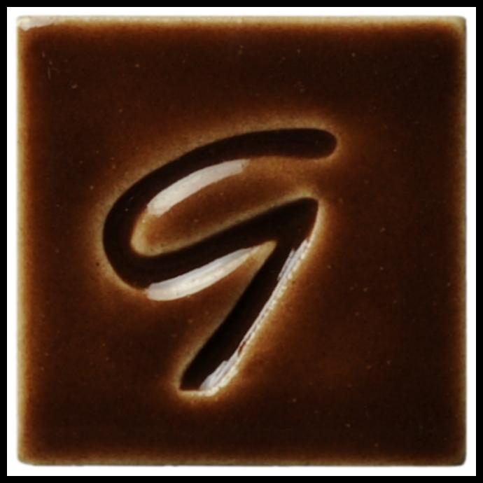 Brown ceramic glaze sample tile featuring an engraved G design, showcasing the texture and color variations in glazing.