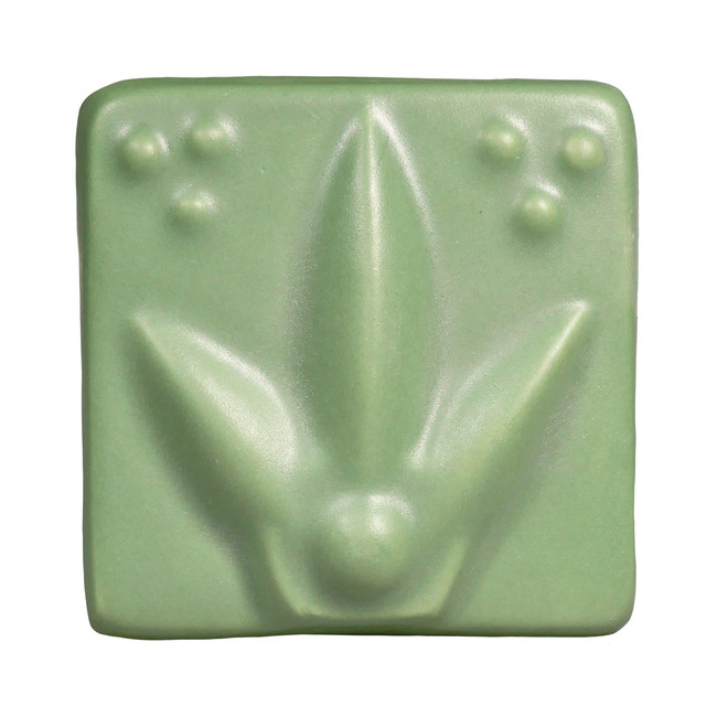A green ceramic tile featuring a floral design with three raised dots, showcasing glazing techniques for pottery.