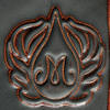 Detail of a ceramic stamp featuring a stylized letter M surrounded by decorative flame-like elements in orange and black.