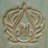 Ceramic imprint featuring an elegant 'M' surrounded by ornate leaf motifs, highlighting clay decoration techniques.