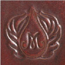 Detail of a textured red glaze featuring an embossed design of the letter M with decorative wings, ideal for pottery finishing.