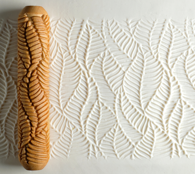 Textured clay surface with a leaf-patterned rolling pin creating an impression in white clay, ideal for ceramic decoration.