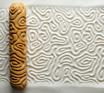 Textured white clay sheet with a patterned wooden impression roller alongside, showcasing decorative techniques for ceramics.