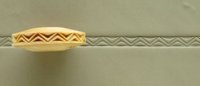 Pottery tool showing a textured design used for decorating clay, with a zigzag pattern impressed onto a gray clay slab.