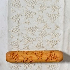 Textured clay slab featuring fish patterns, with a carved wooden roller for imprinting designs in pottery.