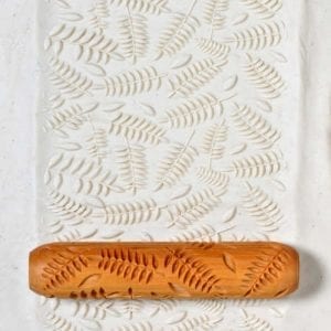 A textured white clay slab with fern patterns, accompanied by an ornamental rolling pin used for ceramic decorating.