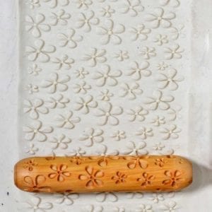 Textured clay slab with flower pattern created using a wooden rolling pin; ideal for ceramics projects and decoration.