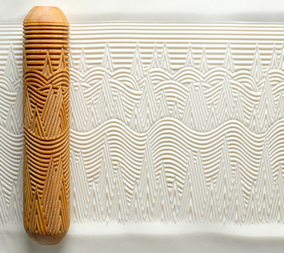 A textured clay surface features intricate wavy patterns, created with a ceramic impression roller.