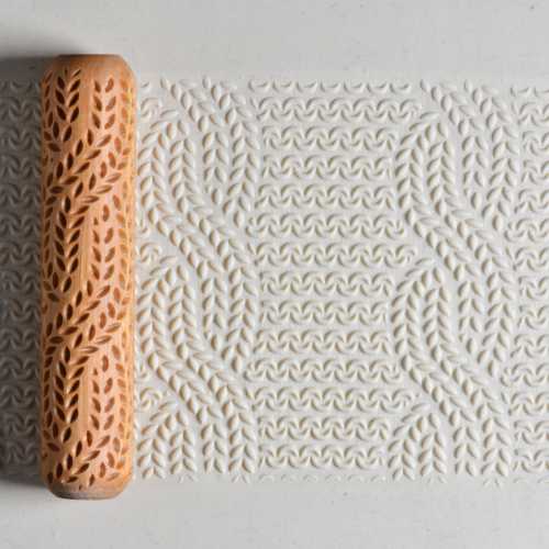 Textured clay roller with leaf design, creating an imprint on white clay surface for pottery decoration.