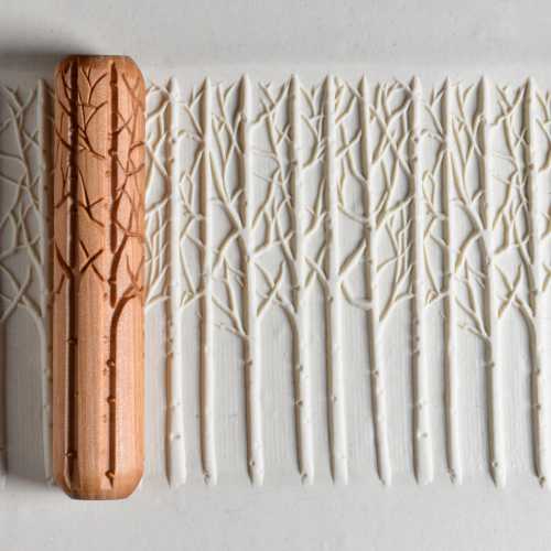 Wooden texture roller stamp creating a forest pattern on white clay, demonstrating decorative techniques for ceramics.