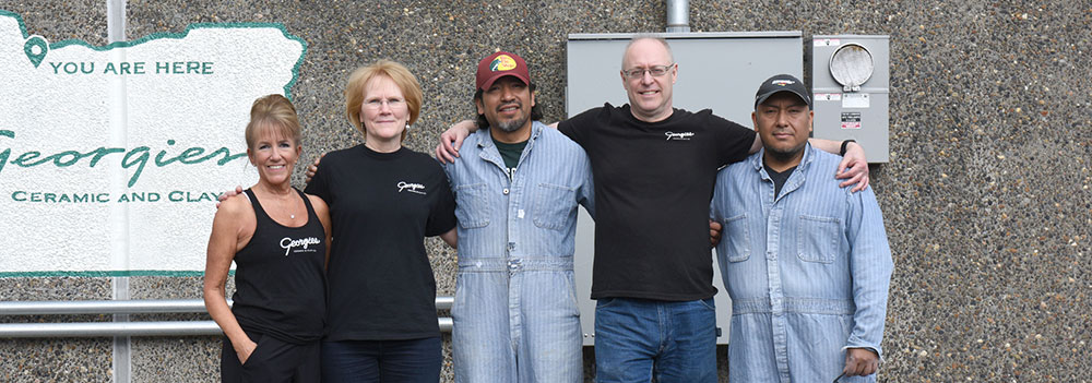 Group of five Georgies Ceramic employees posing in front of the company sign, promoting a welcoming studio atmosphere.