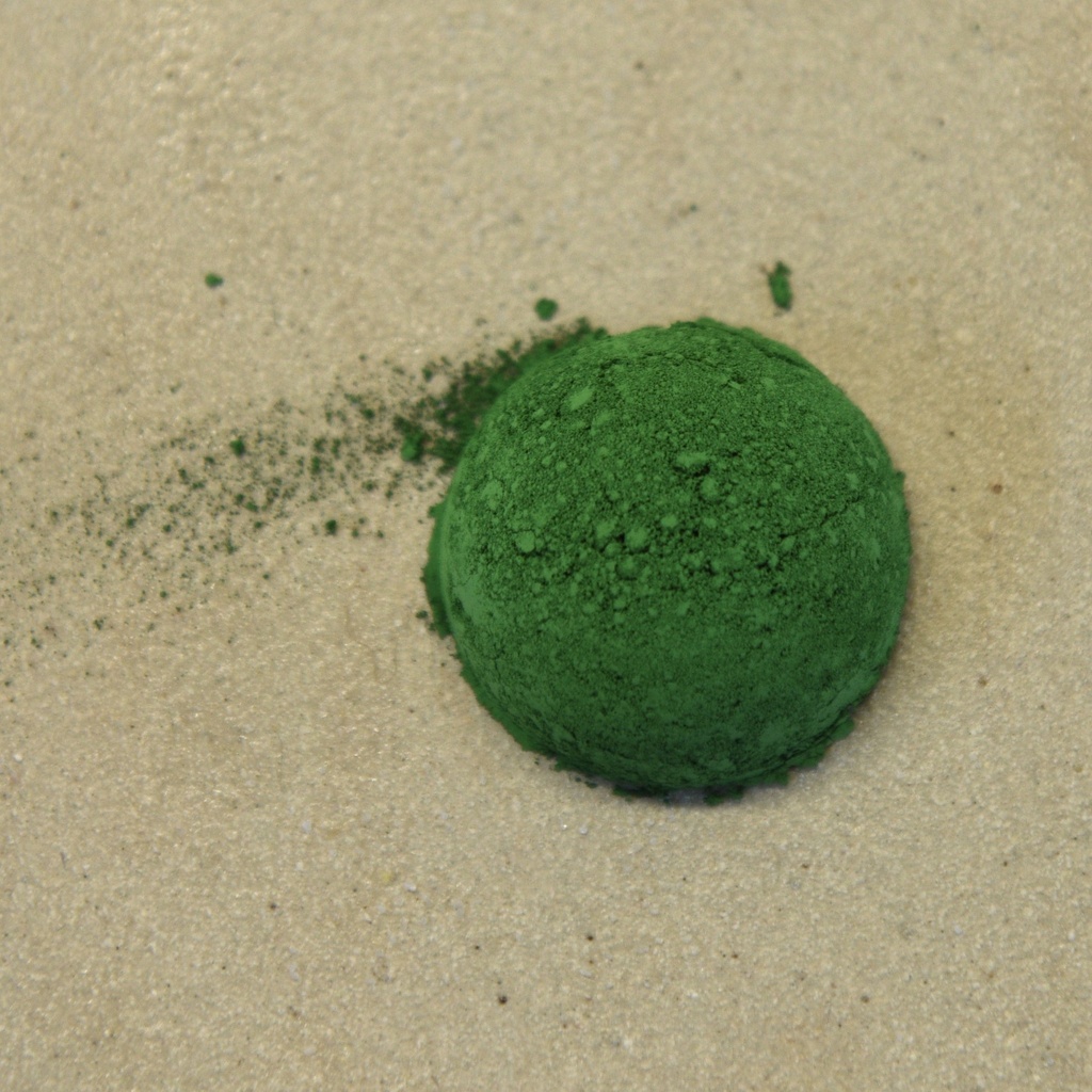 Bright green dry pigment powder on a sandy surface, suitable for ceramic glazes and decorative techniques.