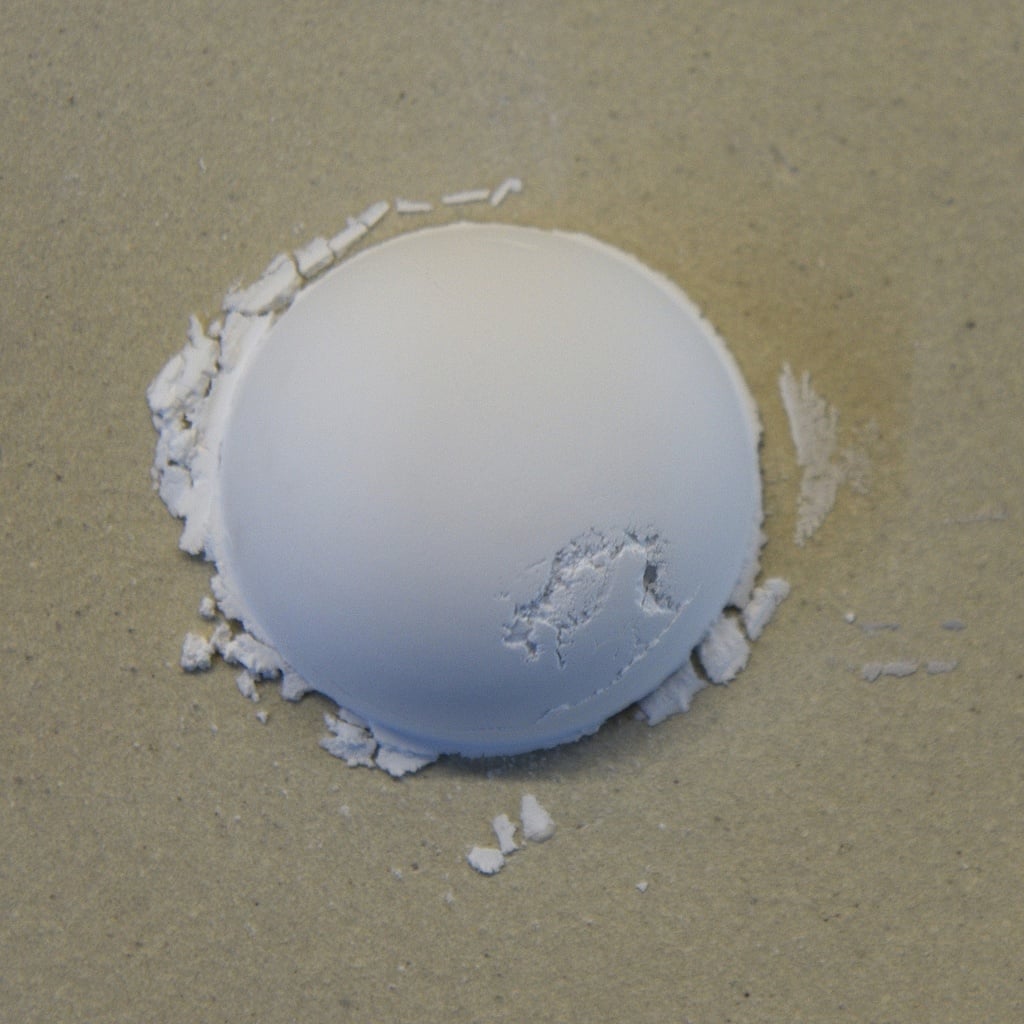 A smooth, white clay sphere rests on a textured surface, surrounded by fine clay dust, showcasing the shaping process.