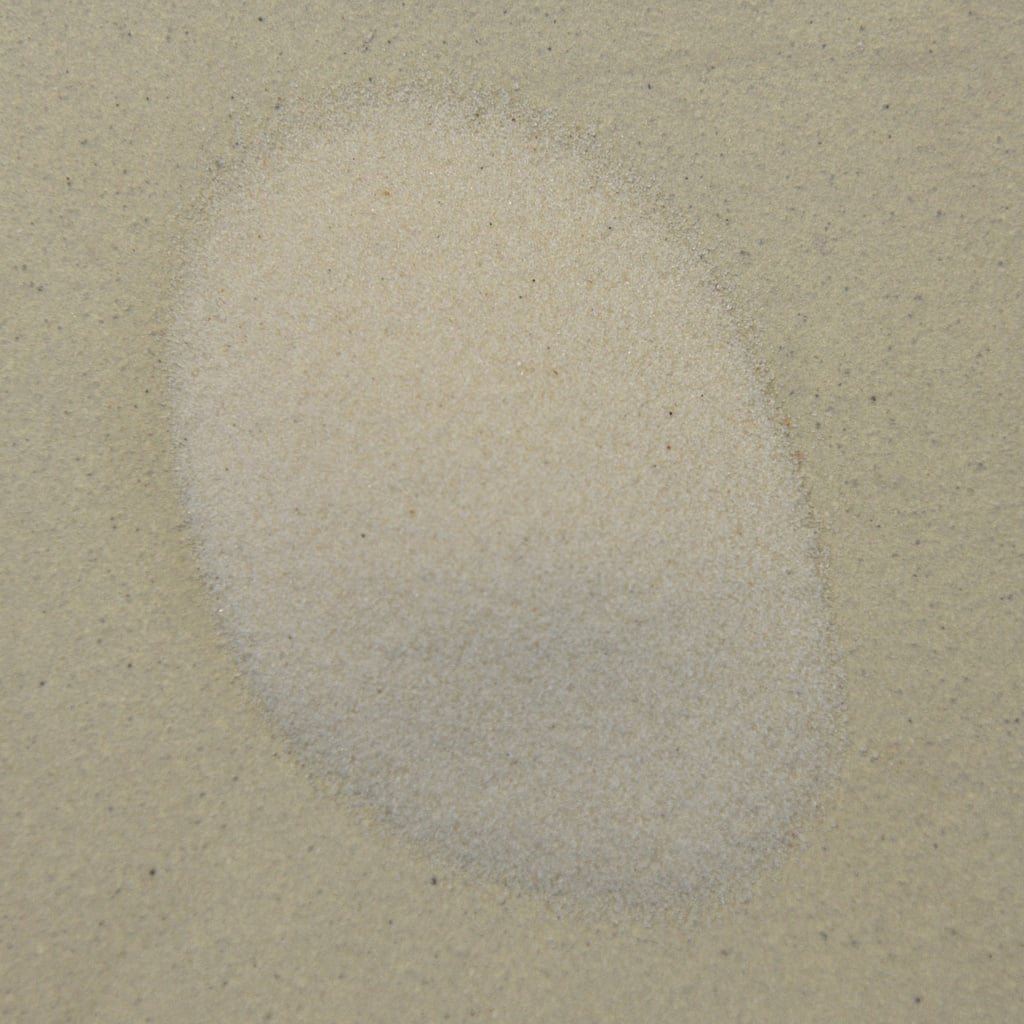 Fine grain sand arranged in an oval shape on a light-colored surface, showcasing texture and consistency for ceramic projects.