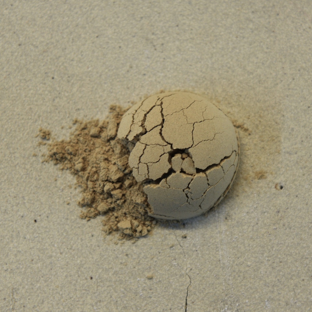 Cracked clay ball on a work surface, showcasing natural texture and uneven color, ideal for ceramics or sculpture applications.