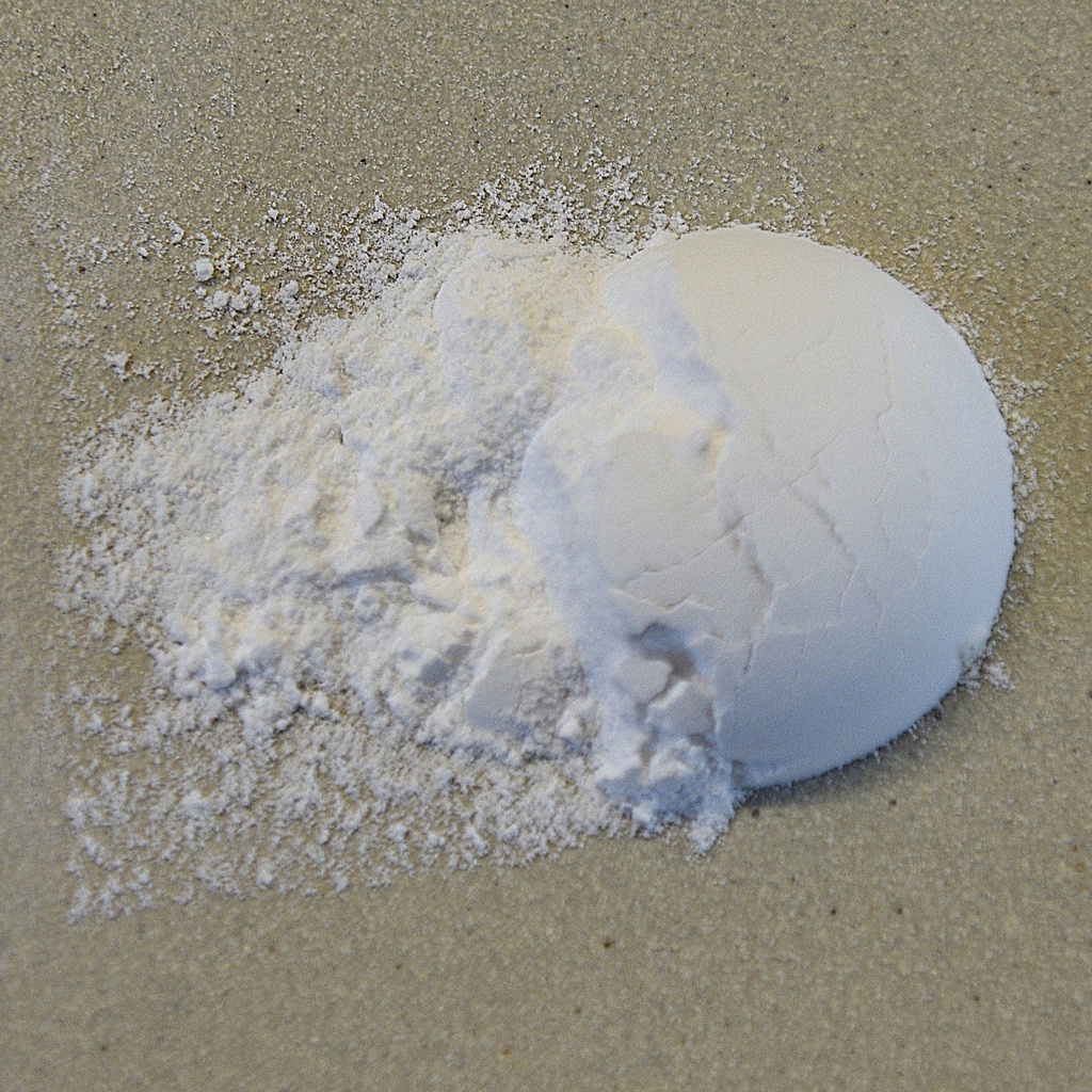 A pile of fine white clay powder spilled beside a smooth, spherical chunk of clay on a neutral background.