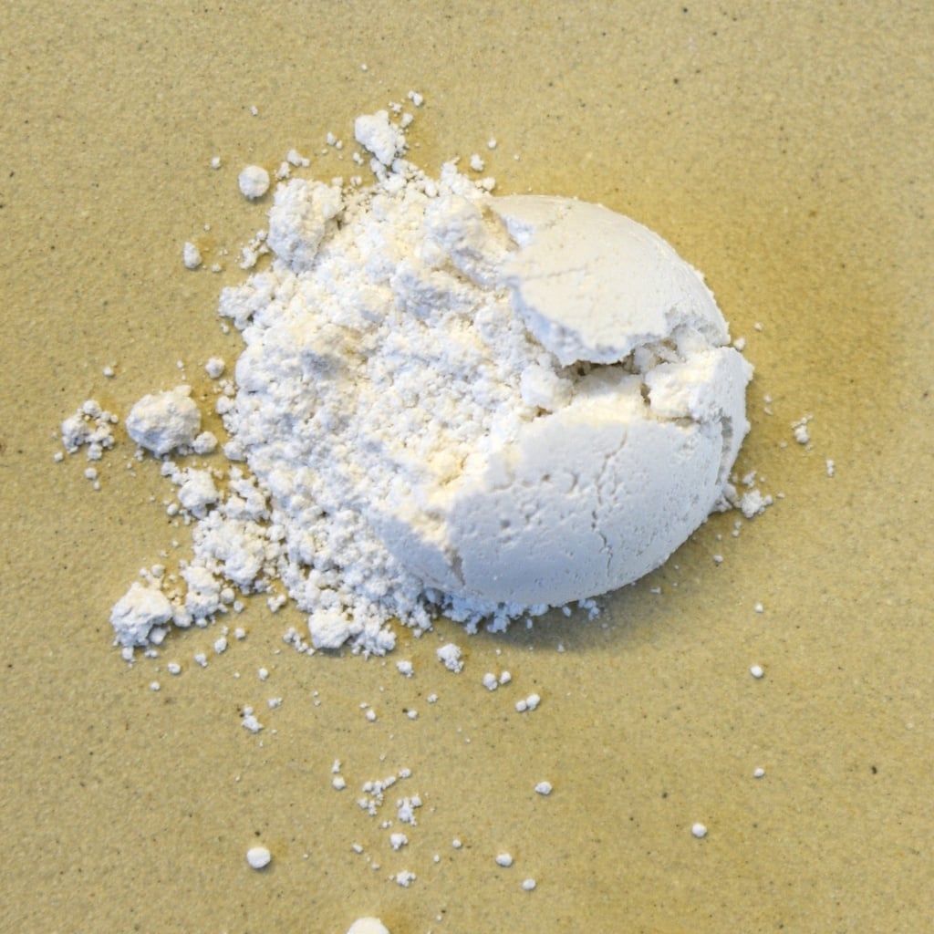 White clay powder scattered on a beige surface, showcasing texture and ready for use in pottery and ceramic projects.