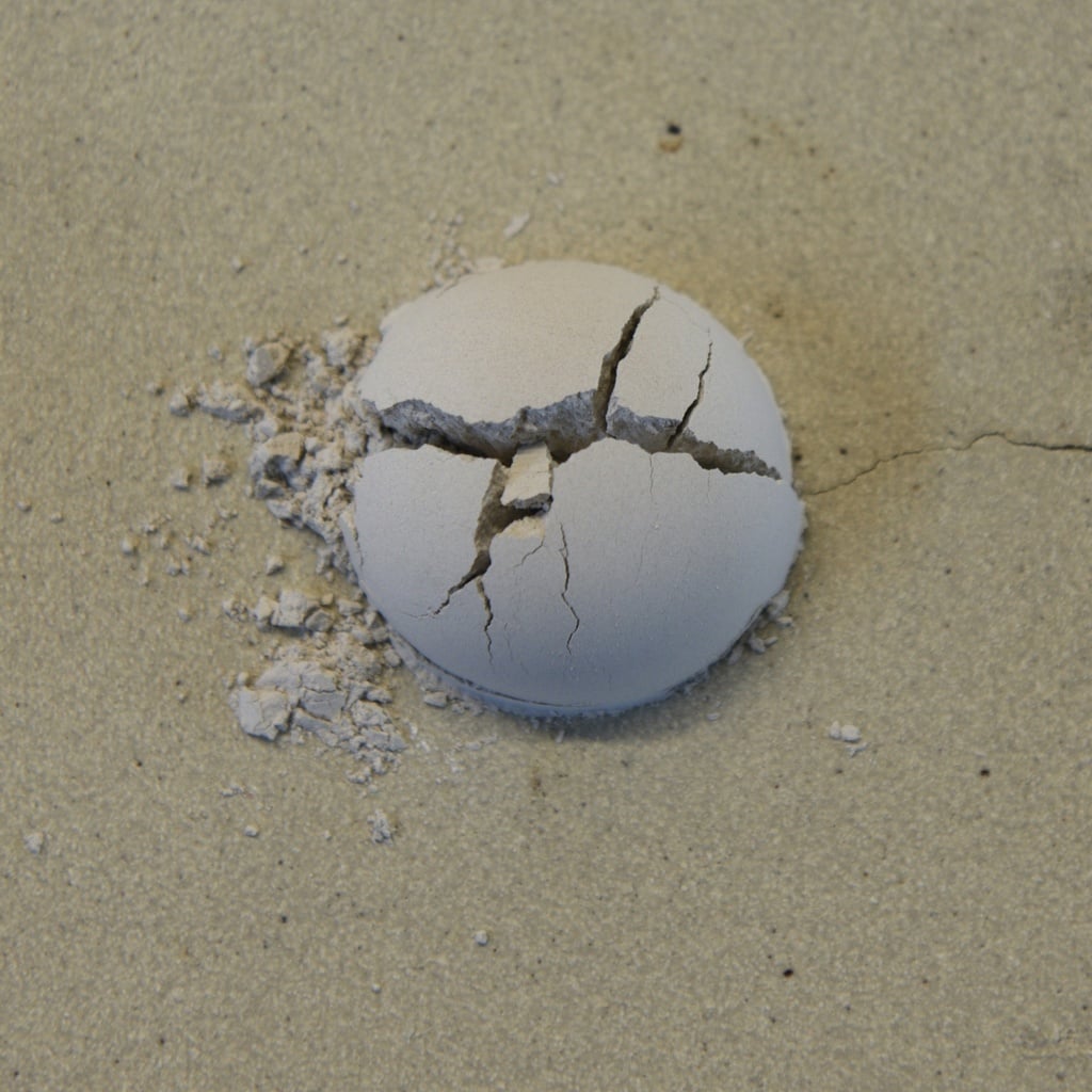 Cracked, unglazed ceramic ball on sandy surface, illustrating pottery clay's drying process at Georgies Ceramic & Clay Company.