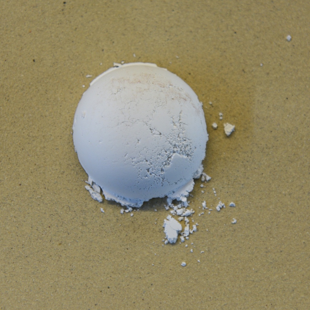 White ceramic ball of clay powder on a textured surface, illustrating raw material used for sculpting and pottery.
