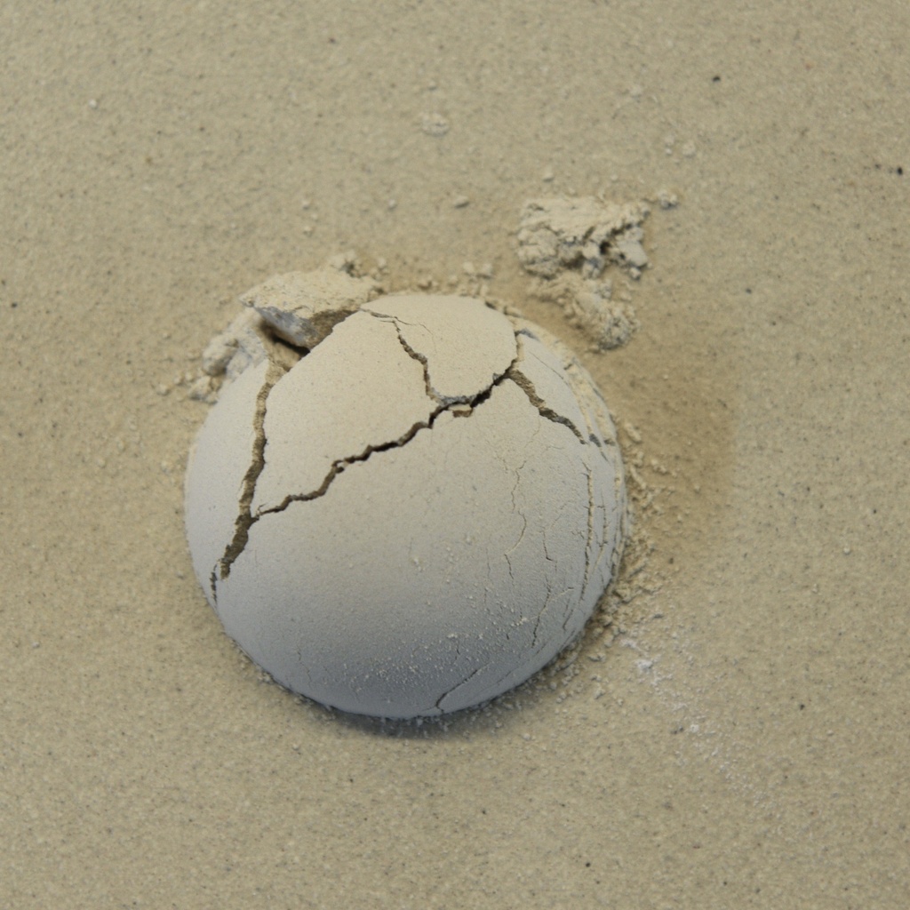 Cracked clay sphere partially embedded in fine, sandy clay, demonstrating drying effects in ceramic sculpture processes.